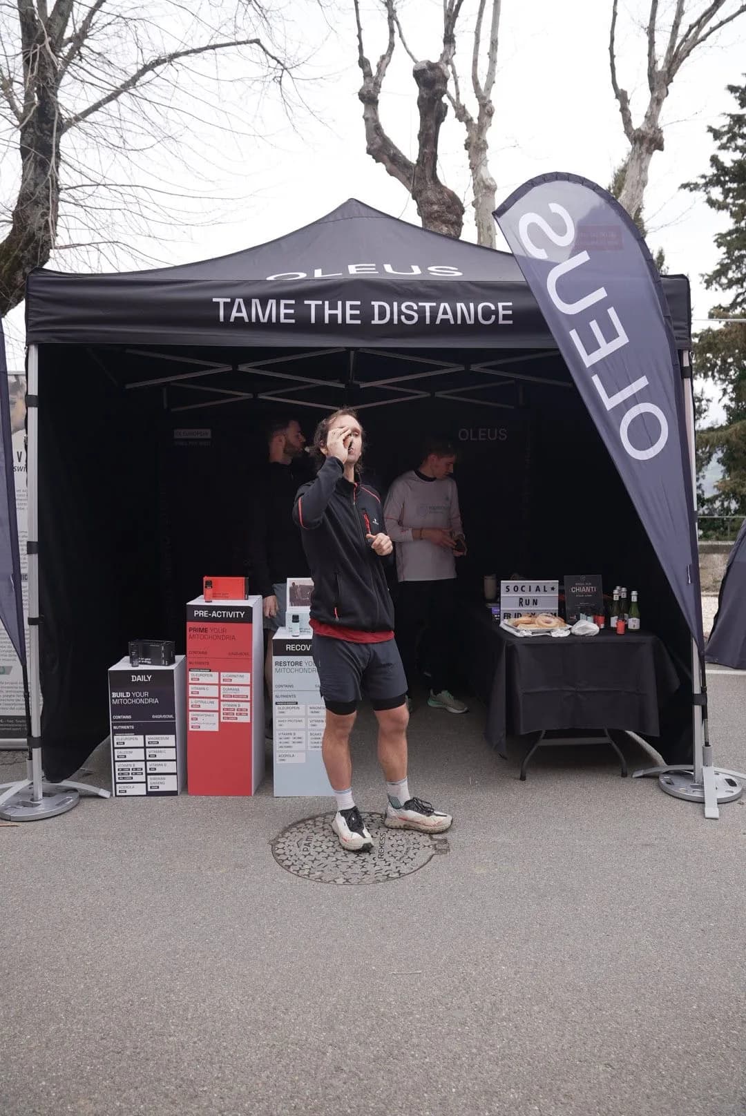 The OLEUS Tame the distance tent at a lakeside race, with a runner taking a shot in front of the product display