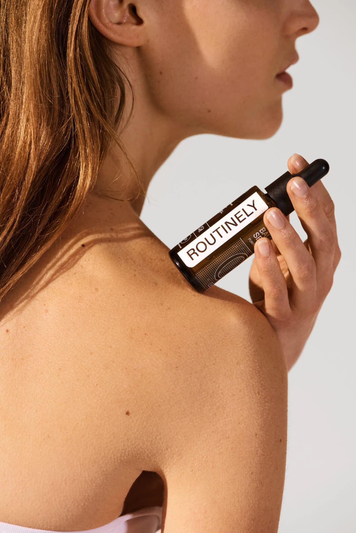 A woman holding a bottle of Routinely serum against her shoulder
