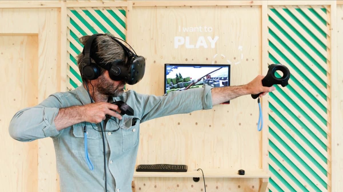 A player in a VR headset with controllers at the plywood I want to PLAY booth