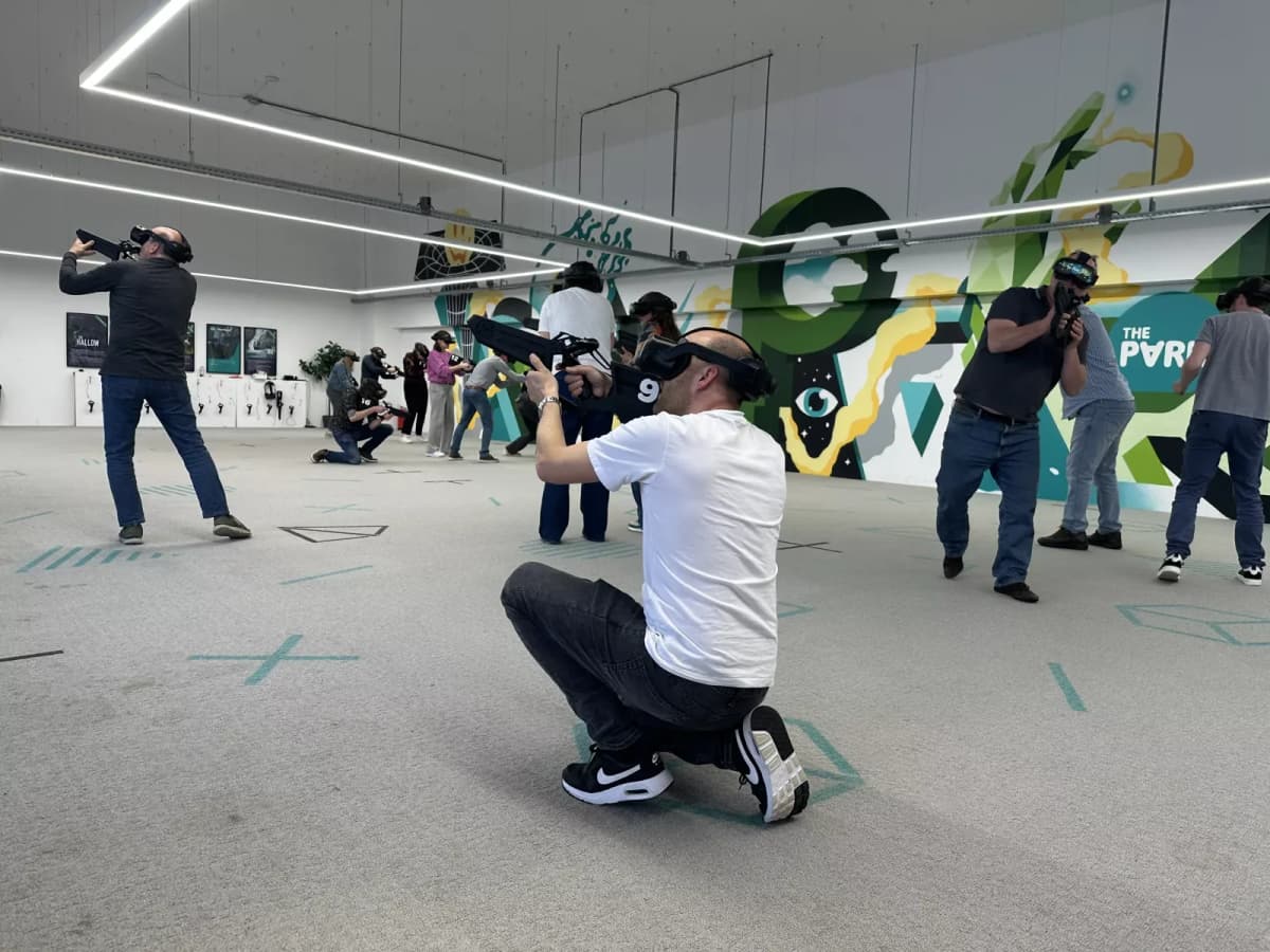 Players in VR headsets with blasters in the arena in front of The Park mural