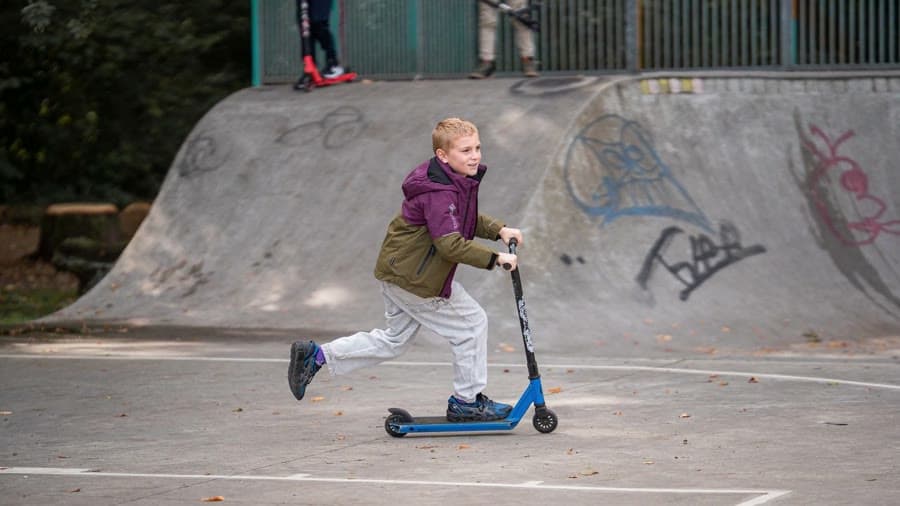 A kid in a Gore-Tex jacket on a scooter in a skate park